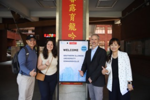 A group of people standing in front of a sign Description automatically generated